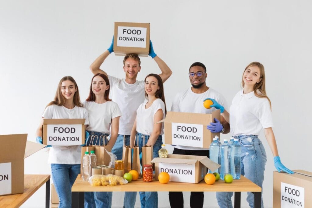 Four women and two men packing food into boxes on a table for donation